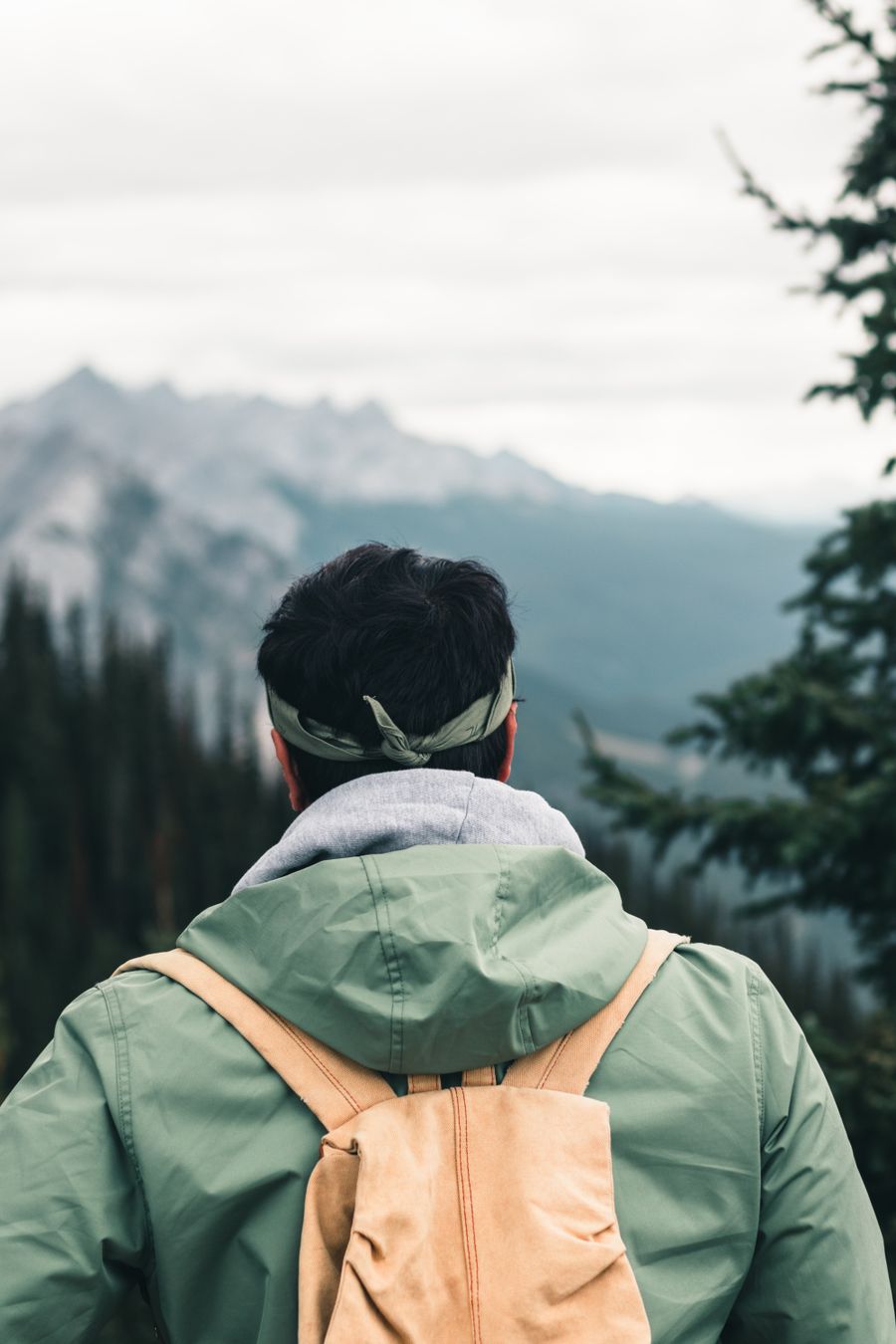 a man in green jacket carrying a brown backpack — Rainy-day backup plan: indoor attractions researched from the hostel bunk.