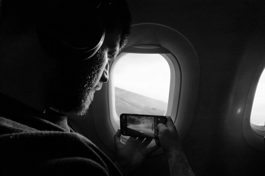 Man taking photo out of airplane window, capturing wing view with smartphone. — Festivals à Tunisia : point de rendez-vous épinglé, amis retrouvés dans la foule.