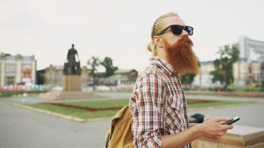 Hipster with a beard and sunglasses in a city square holding a smartphone. — Chasse aux souvenirs à DR Congo avec conversion de devises en direct dans la poche.