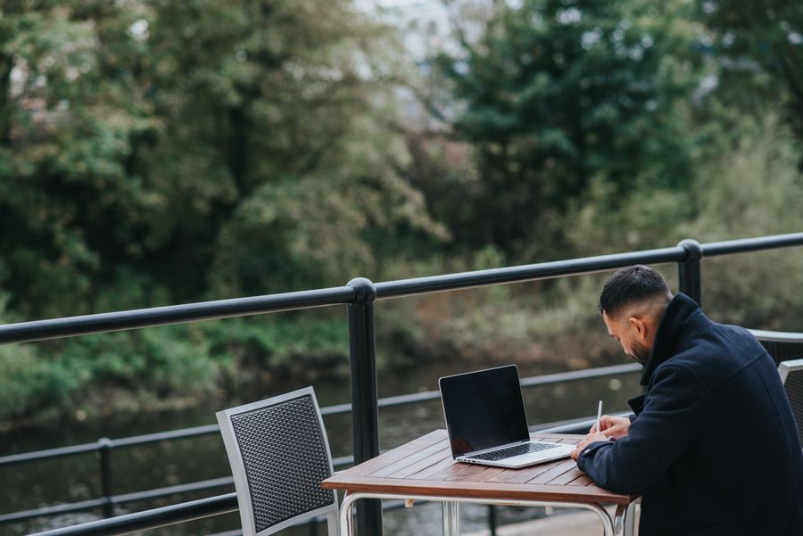 anonymous ethnic worker writing near laptop on cafe terrace — Low-Data Alert: the fastest way to turn a vague travel question into a next step.