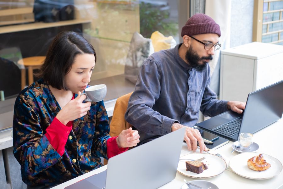 man and woman sitting in a cafe and using laptops while having a coffee and cake — Night markets and late trains — connected the whole way through.