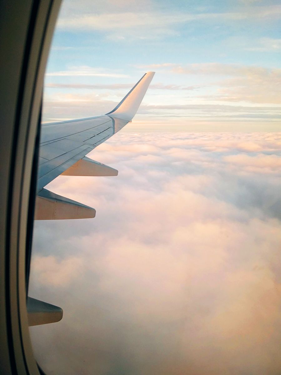 wing of aircraft flying over clouds at sundown