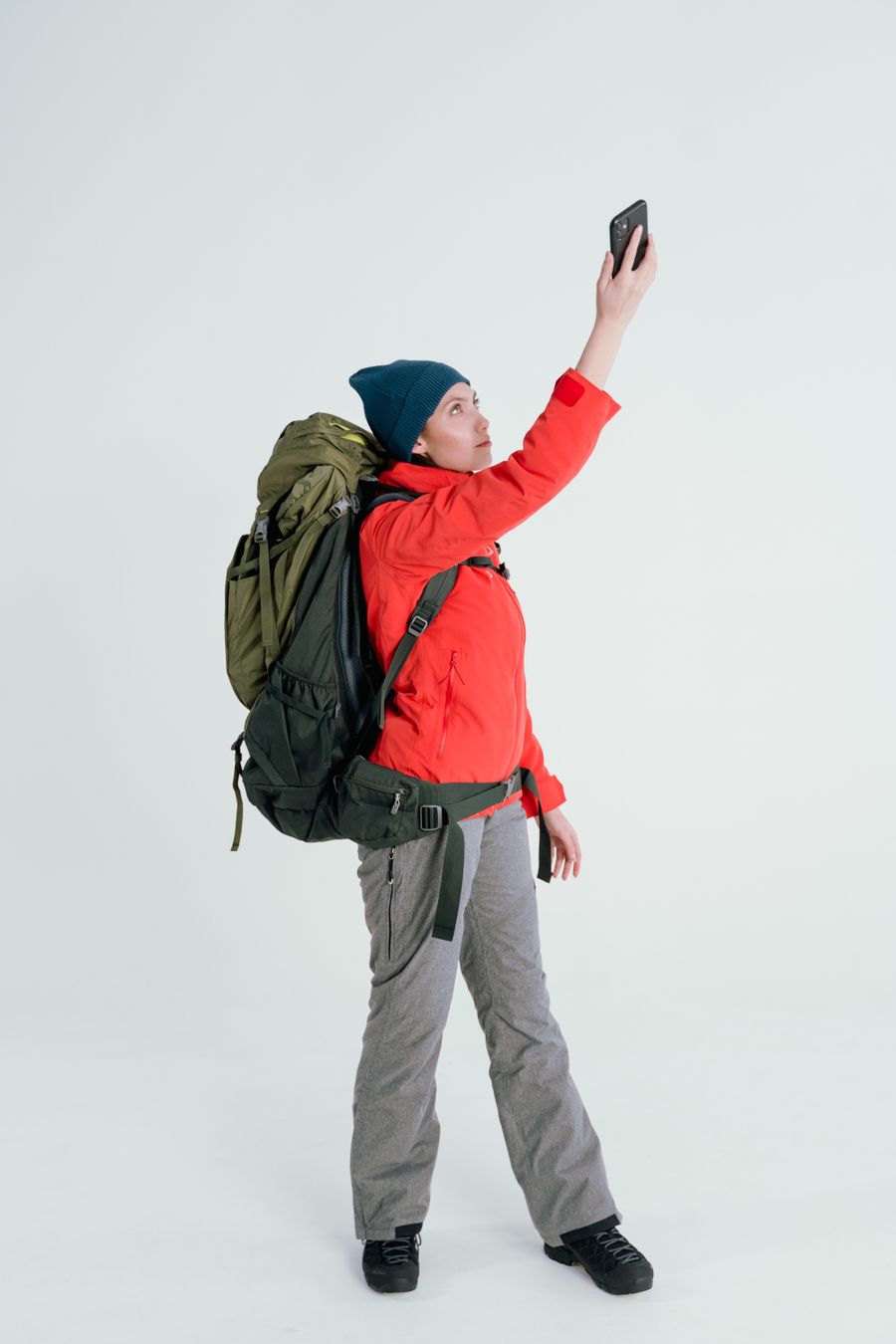 Young woman backpacker taking a selfie on a white background, dressed in outdoor gear. — Le hall des arrivées de Côte d'Ivoire : en ligne avant le tapis à bagages, à chaque fois.