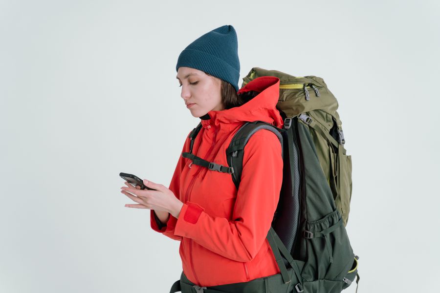 A woman in outdoor gear checking her smartphone, ready for adventure. — Le Tele Agent vous guide en direct dans l'installation si quelque chose coince.