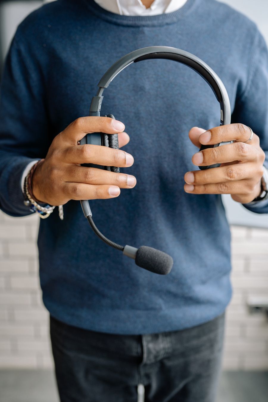 close up shot of a person in blue sweater holding a black headset — Changelog: Le badge de la conférence : billet QR scanné, programme synchronisé.