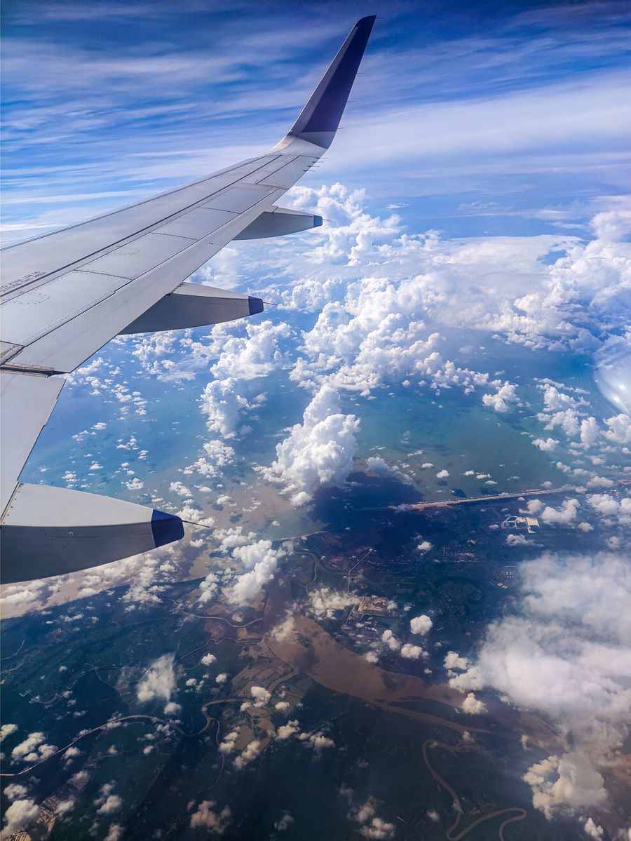 photo of an airplane wing over white clouds — The window seat office: emails sent somewhere over the ocean.